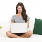 Beautiful woman on a sofa working with a laptop, isolated in white